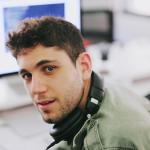 man in green shirt with headphones around neck, looking at camera